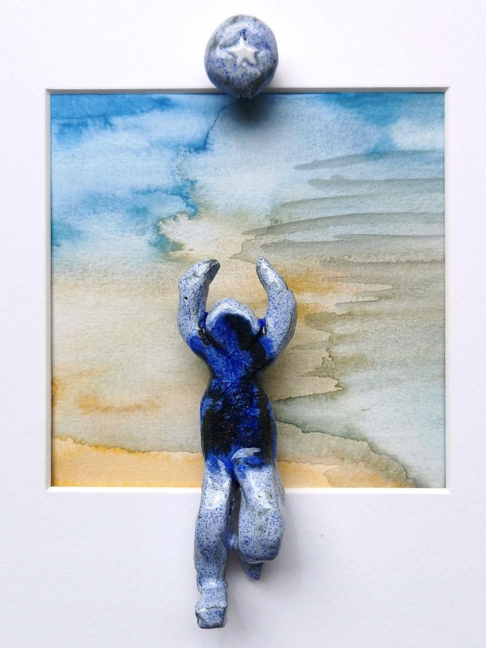 "Strandurlaub" 9/2025, 10,5 x 4 x 3,3 cm, schwarzer und weißer Ton glasiert mit Tonperle auf Aquarell, gerahmt (25 x25 cm)